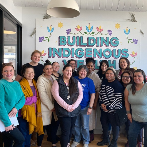 Photo of Mni Sota Fund grantee in front of a sign that says Building Indigenous Wealth